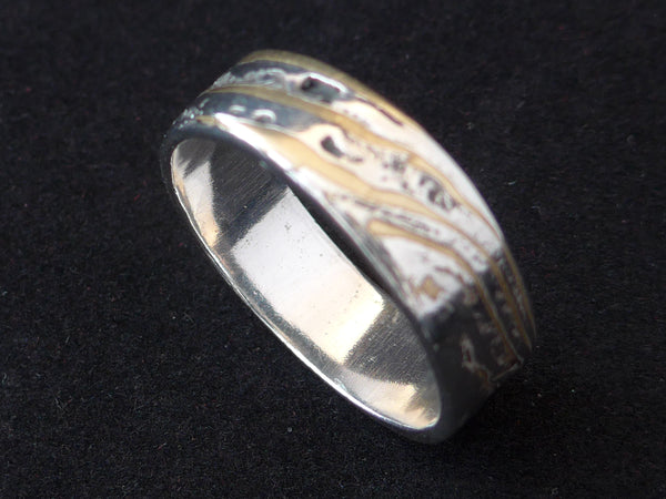 Deze stoere ring is gemaakt van Mokume Gane. Dit is een bewerkelijke Japanse smeedtechniek waarbij laagjes verschillende metalen, in dit geval zilver en koper, met elkaar versmelten onder hoge temperaturen. In het Japans betekent mokume houtnerf en gane betekent metaal. 