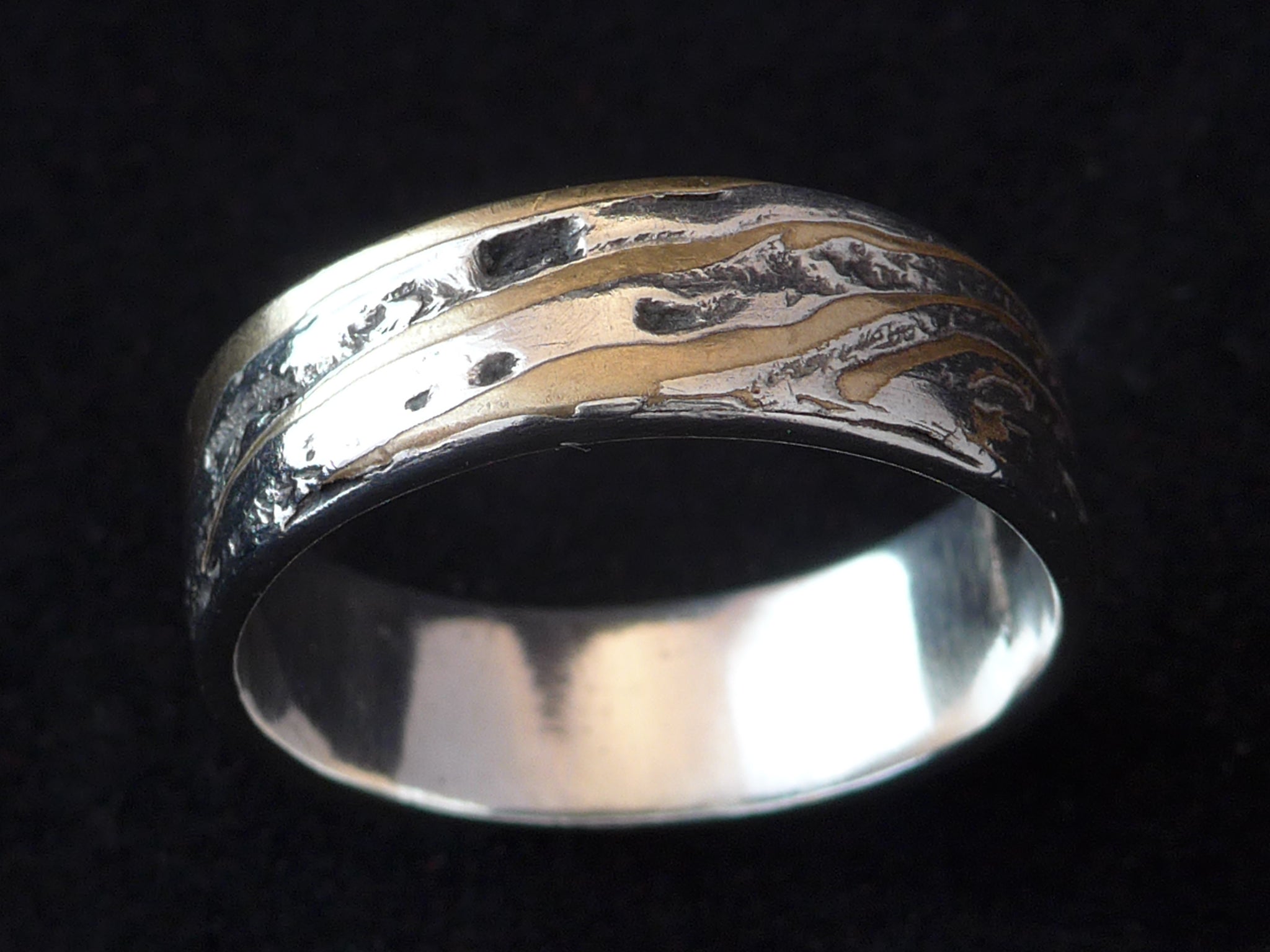 Deze stoere ring is gemaakt van Mokume Gane. Dit is een bewerkelijke Japanse smeedtechniek waarbij laagjes verschillende metalen, in dit geval zilver en koper, met elkaar versmelten onder hoge temperaturen. In het Japans betekent mokume houtnerf en gane betekent metaal. 