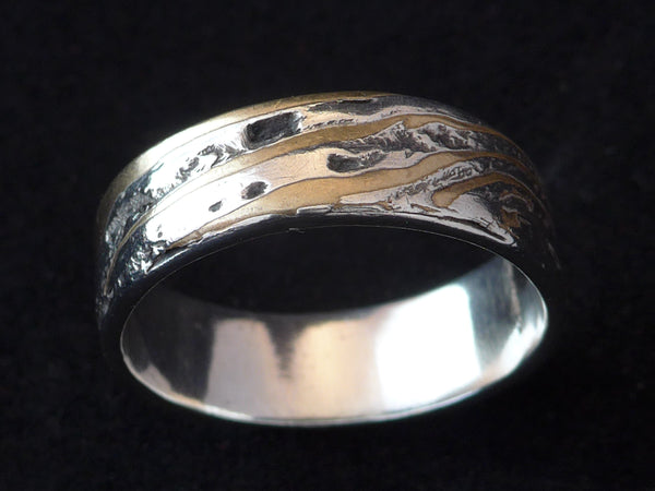 Deze stoere ring is gemaakt van Mokume Gane. Dit is een bewerkelijke Japanse smeedtechniek waarbij laagjes verschillende metalen, in dit geval zilver en koper, met elkaar versmelten onder hoge temperaturen. In het Japans betekent mokume houtnerf en gane betekent metaal. 