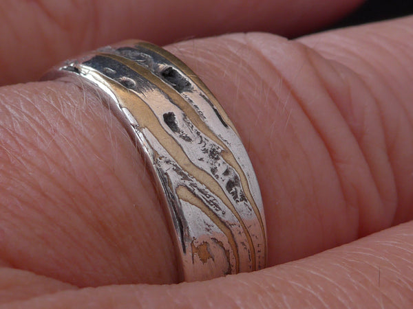 Deze stoere ring is gemaakt van Mokume Gane. Dit is een bewerkelijke Japanse smeedtechniek waarbij laagjes verschillende metalen, in dit geval zilver en koper, met elkaar versmelten onder hoge temperaturen. In het Japans betekent mokume houtnerf en gane betekent metaal. 