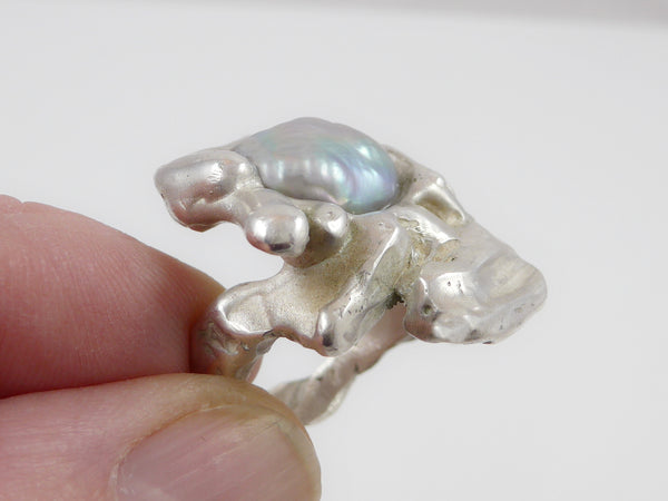 Een flinke, stoere ring aan je hand met daarop een prachtig warmglanzende, blauwgrijze barokke zoetwaterparel is altijd iets bijzonders. De ring is gegoten en daardoor massief maar toch niet zwaar. De vorm is organisch en vloeiend. 